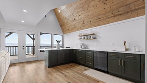 A modern kitchen with dark cabinets, wooden flooring, and a view through large windows. - Mountain’s Edge by Appalachian A-Frames, Mountain View, Hot Tub, WiFi (Trenton)