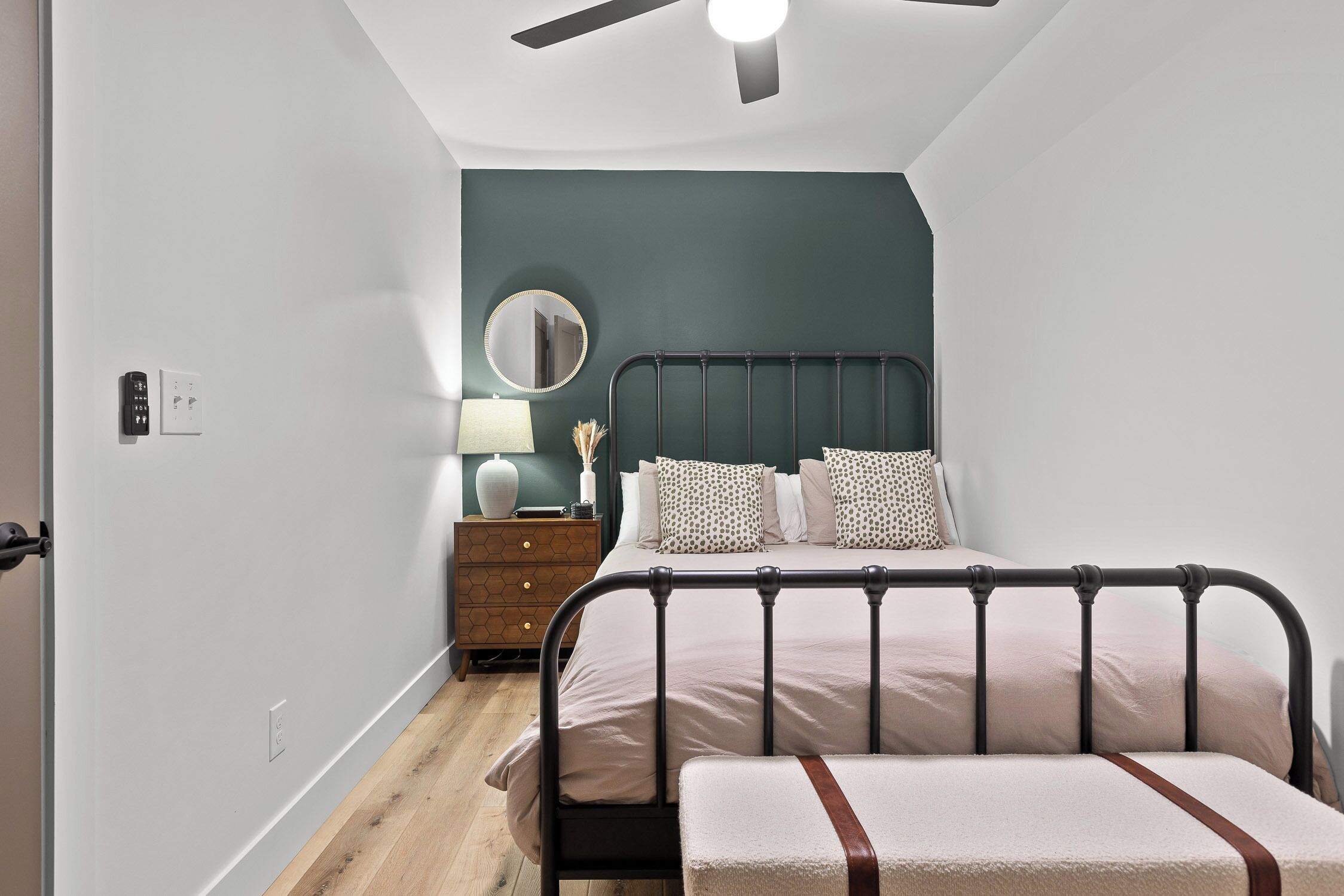 Een slaapkamer met een bed, nachtkastje, lamp en plafondventilator.