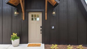 A dark wooden building with a beige door, a potted plant, and a welcome mat. - Mountain’s Edge by Appalachian A-Frames, Mountain View, Hot Tub, WiFi (Trenton)