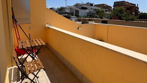A balcony with a yellow wall, a wooden folding table, and a red chair. - Mungo in Fiumicino With 1 Bedrooms and 1 Bathrooms (Fiumicino)