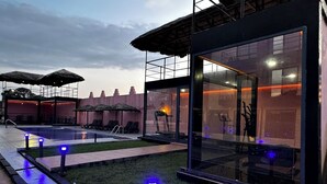 Un área de piscina moderna al aire libre con paredes de vidrio, sillones de descanso y sombrillas.