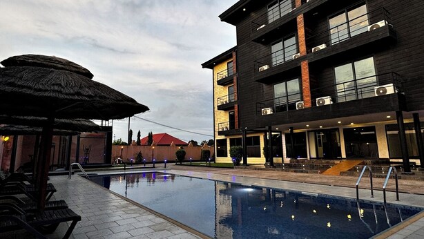 Un edificio moderno con piscina, mobiliario exterior y una estructura de techo de paja.