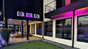 Un edificio moderno con amplios ventanales, un espacio al aire libre techado y tres unidades de aire acondicionado.