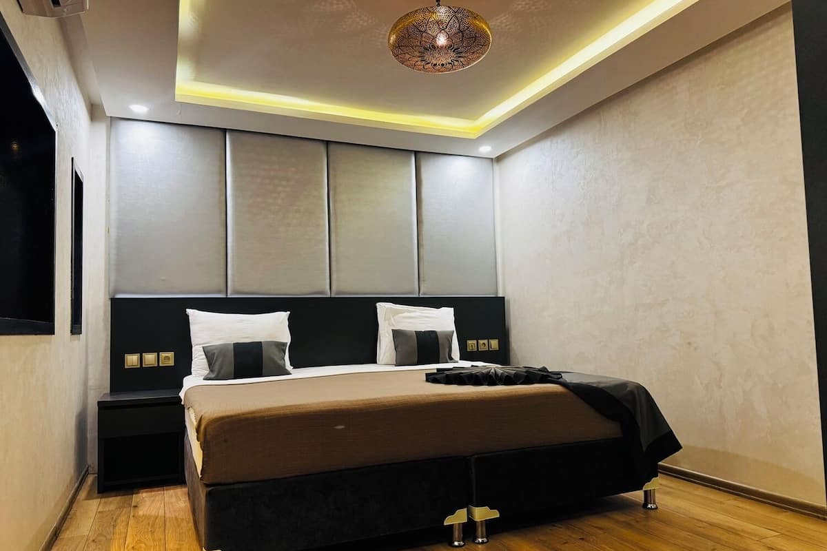A modern bedroom with a large bed, a black nightstand, a bedside table, and a ceiling light fixture.