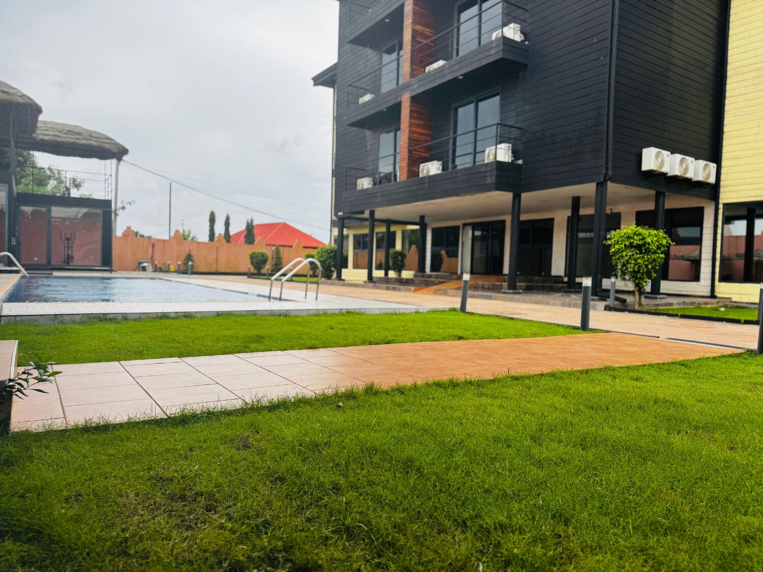 A modern building with a swimming pool, a covered patio area, and a well-maintained lawn.