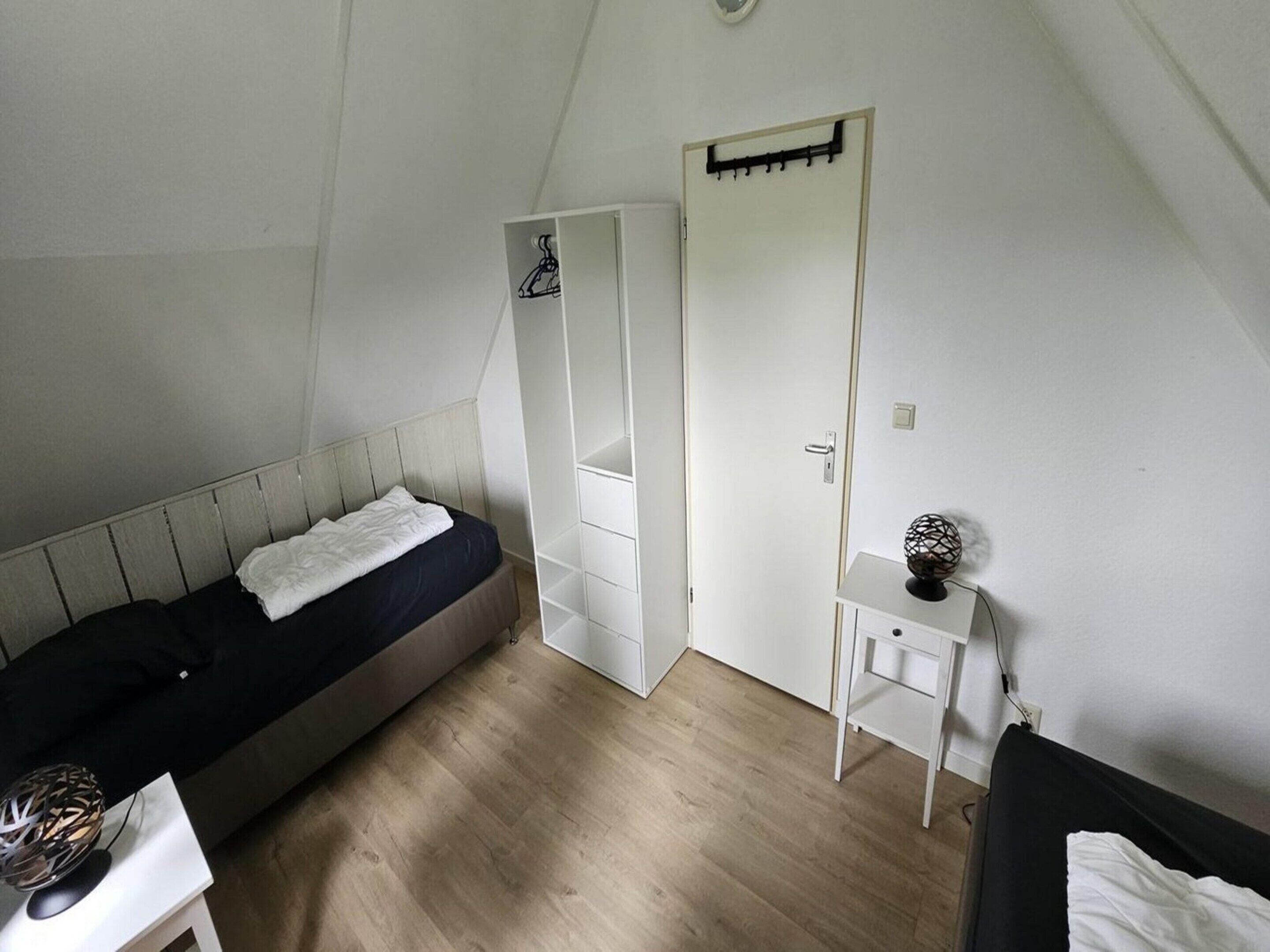 A bedroom with a bed, a wardrobe, a bedside table, and a small desk.