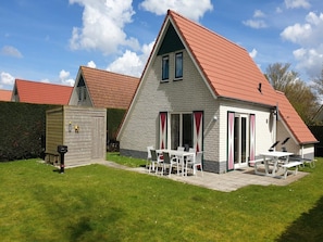 A two-story house with a red roof, a patio with outdoor furniture, and a small shed.