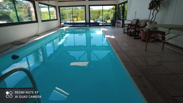 An indoor swimming pool with clear glass walls, wooden ceiling beams, and a view of greenery outside. - 4 BEDROOM COUNTRY HOUSE INDOOR POOL and SAUNA
8 PEOPLE PRIVATE (Saint-Augustin)