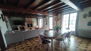 A dining area with a hexagonal tile floor, a round table with chairs, a brick fireplace, and a television above the fireplace. - 4 BEDROOM COUNTRY HOUSE INDOOR POOL and SAUNA
8 PEOPLE PRIVATE (Saint-Augustin)