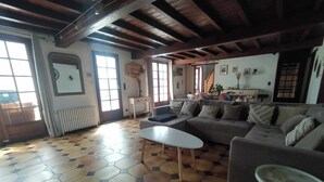 A spacious living room with a large sofa, a coffee table, and a small side table. The room has a tiled floor with a geometric pattern and wooden beams on the ceiling. - 4 BEDROOM COUNTRY HOUSE INDOOR POOL and SAUNA
8 PEOPLE PRIVATE (Saint-Augustin)