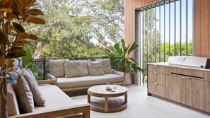 A balcony with a sofa, a round wooden table, and a built-in kitchen area.