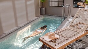 Ein Schwimmbecken mit einer Person, die treibt, einer Liege und einem Topf mit einer Pflanze.