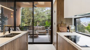 A modern kitchen with a glass door leading to a patio area, a dining set, and a view of greenery.