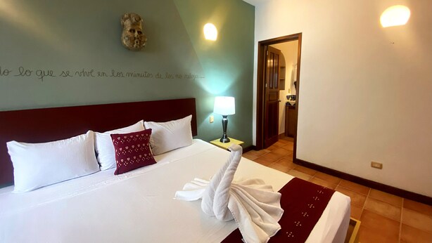 Cama bem arrumada com almofadas brancas e bordô, uma toalha e um objeto decorativo na parede.