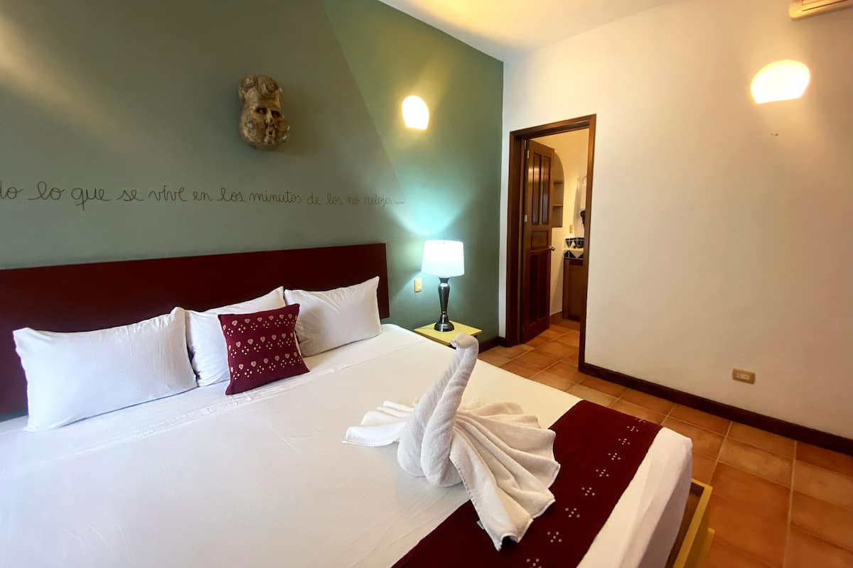 A neatly made bed with white and maroon pillows, a towel, and a decorative wall piece.
