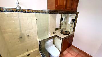 Un baño con ducha de vidrio, inodoro blanco y lavamanos con un elegante revestimiento de azulejos.