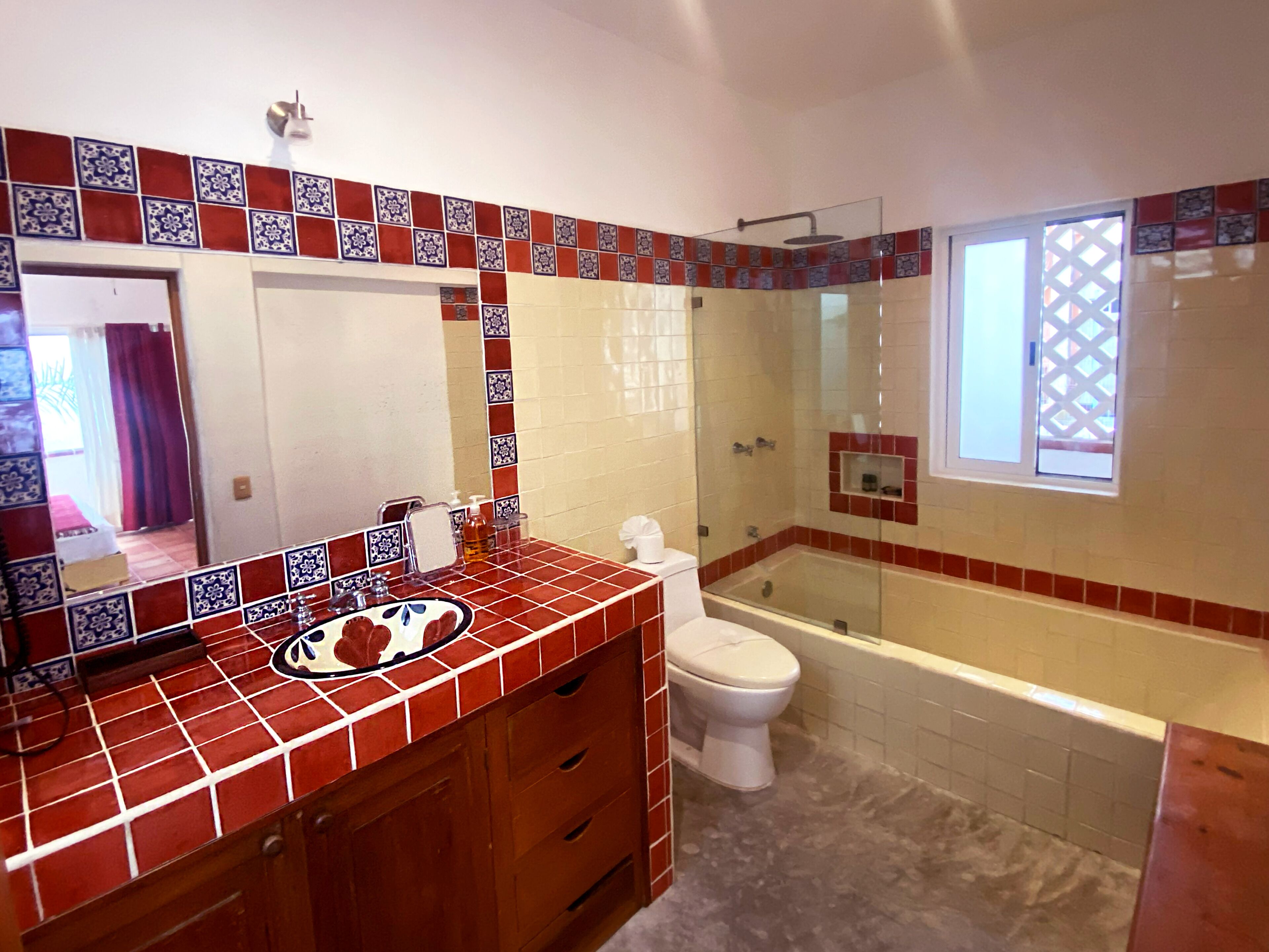 Une salle de bain avec un mur recouvert de carreaux rouges et blancs derrière le lavabo, des toilettes blanches, une douche en verre et une baignoire.