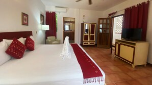 Quarto de hotel com uma cama grande, um ventilador de teto, uma televisão, um guarda-roupa e um banheiro visível através de uma porta aberta.