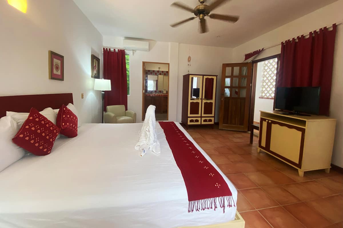 A hotel room with a large bed, a ceiling fan, a TV, a wardrobe, and a bathroom visible through an open door.