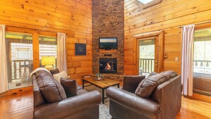 A cozy cabin interior with a stone fireplace, leather sofas, and wooden walls. - Smoky Traditions-Luxury Cabin,Gated,Pools,Mini-golf, Brand New Multi-Game Arcade (Sevierville)