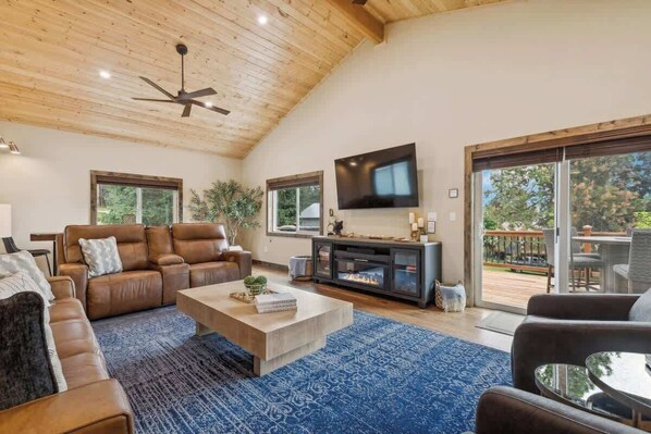 A spacious living room with a high ceiling, leather sofas, a flat-screen TV, and a fireplace.