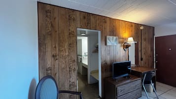 A room with a wooden wall, a desk with a TV, a chair, and a lamp.
