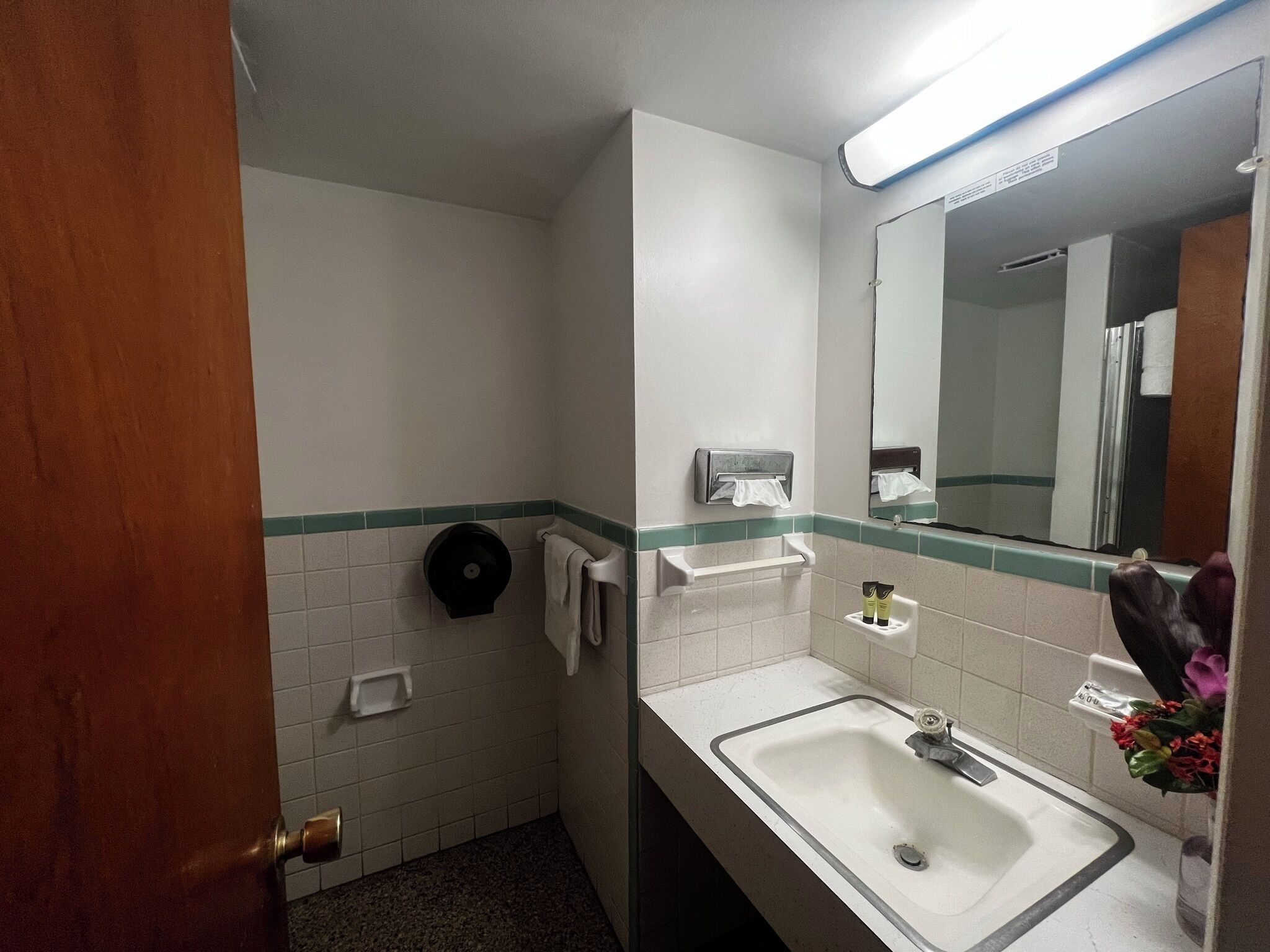A small bathroom with a sink, mirror, towel dispenser, and a toilet paper holder.