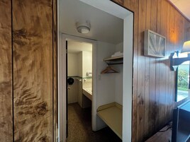 A room with wooden walls, a small kitchenette, a single bed, and a window with a view.