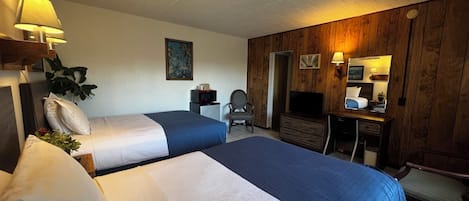 A hotel room with two beds, a desk, a chair, a television, and a mirror.