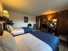 A hotel room with two beds, a desk, a chair, a television, and a mirror.