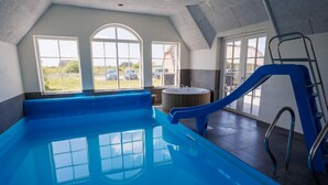 Una piscina interior con un tobogán azul, ventanas amplias y vistas al exterior.
