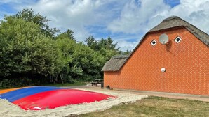 A brick building with a thatched roof, a satellite dish, and a red and blue inflatable slide. - 4 Star Holiday Home in Ulfborg (Ulfborg)