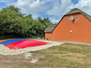 A brick building with a thatched roof, a satellite dish, and a red and blue inflatable slide. - 4 Star Holiday Home in Ulfborg (Ulfborg)