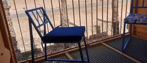 A balcony with a metal railing, a blue chair, and a small table with a patterned tablecloth.