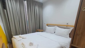 Hotellihuone, jossa on sänky, verhot, pieni pöytä ja televisio.