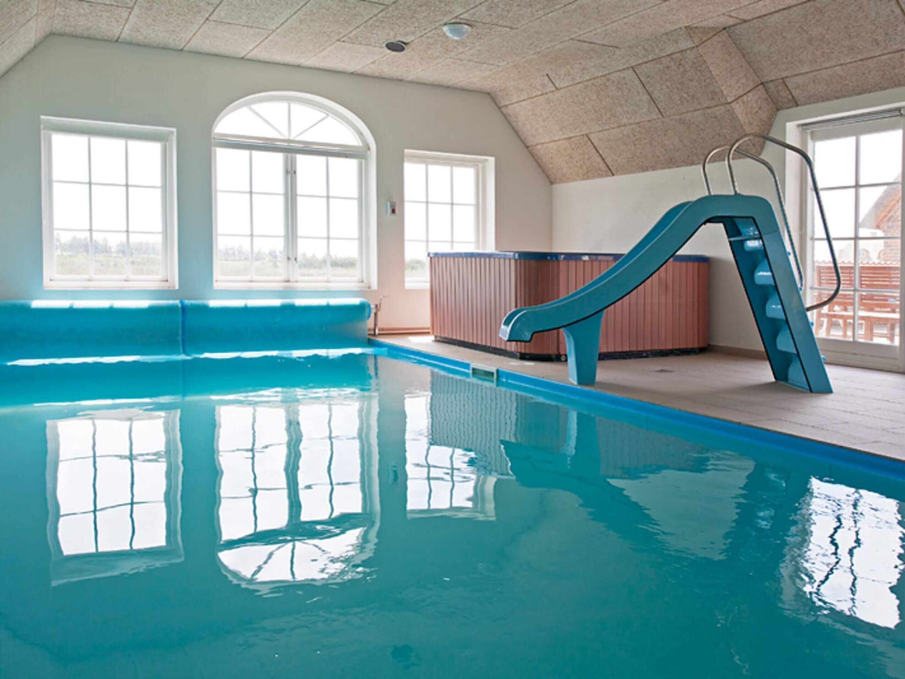 An indoor swimming pool with a slide, large windows, and a view of the outside. - 4 Star Holiday Home in Ulfborg (Ulfborg)