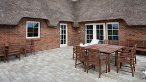A brick building with a thatched roof, a patio with a table and chairs, and a brick floor. - 4 Star Holiday Home in Ulfborg (Ulfborg)