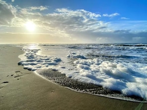 Una playa con olas, huellas y cielo despejado.