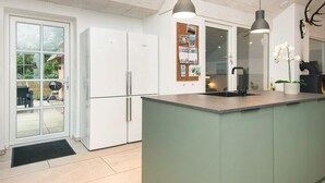 A modern kitchen with a central island, white cabinets, and a corkboard with photos. - Luxury Pool House Near Sea - By Traum Ferienwohnungen (Ulfborg)