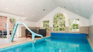 An indoor swimming pool with a slide, a hot tub, and a view of greenery through large windows. - Luxury Pool House Near Sea - By Traum Ferienwohnungen (Ulfborg)
