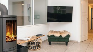 A modern living room with a fireplace, a television mounted on the wall, a wooden table, and a green sofa. - Luxury Pool House Near Sea - By Traum Ferienwohnungen (Ulfborg)