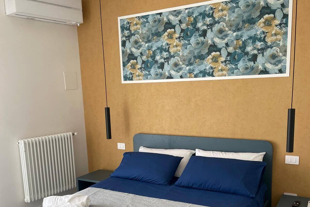 Une chambre à coucher moderne, avec un lit, un radiateur, un appareil de climatisation et une grande œuvre d’art florale accrochée au mur.
