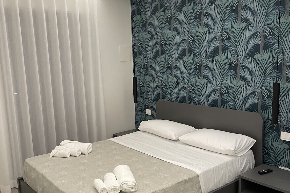 Une chambre moderne avec un lit, une table de chevet, un climatiseur fixé au mur et une fenêtre avec des stores.