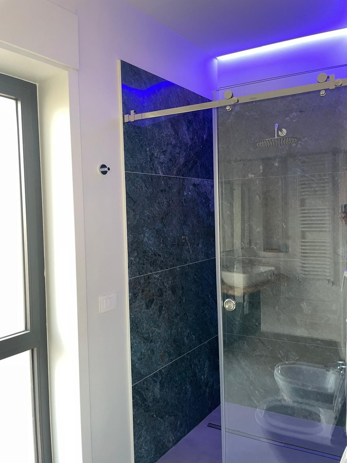 A modern bathroom with dark marble tiles, a glass shower enclosure, and a visible toilet.