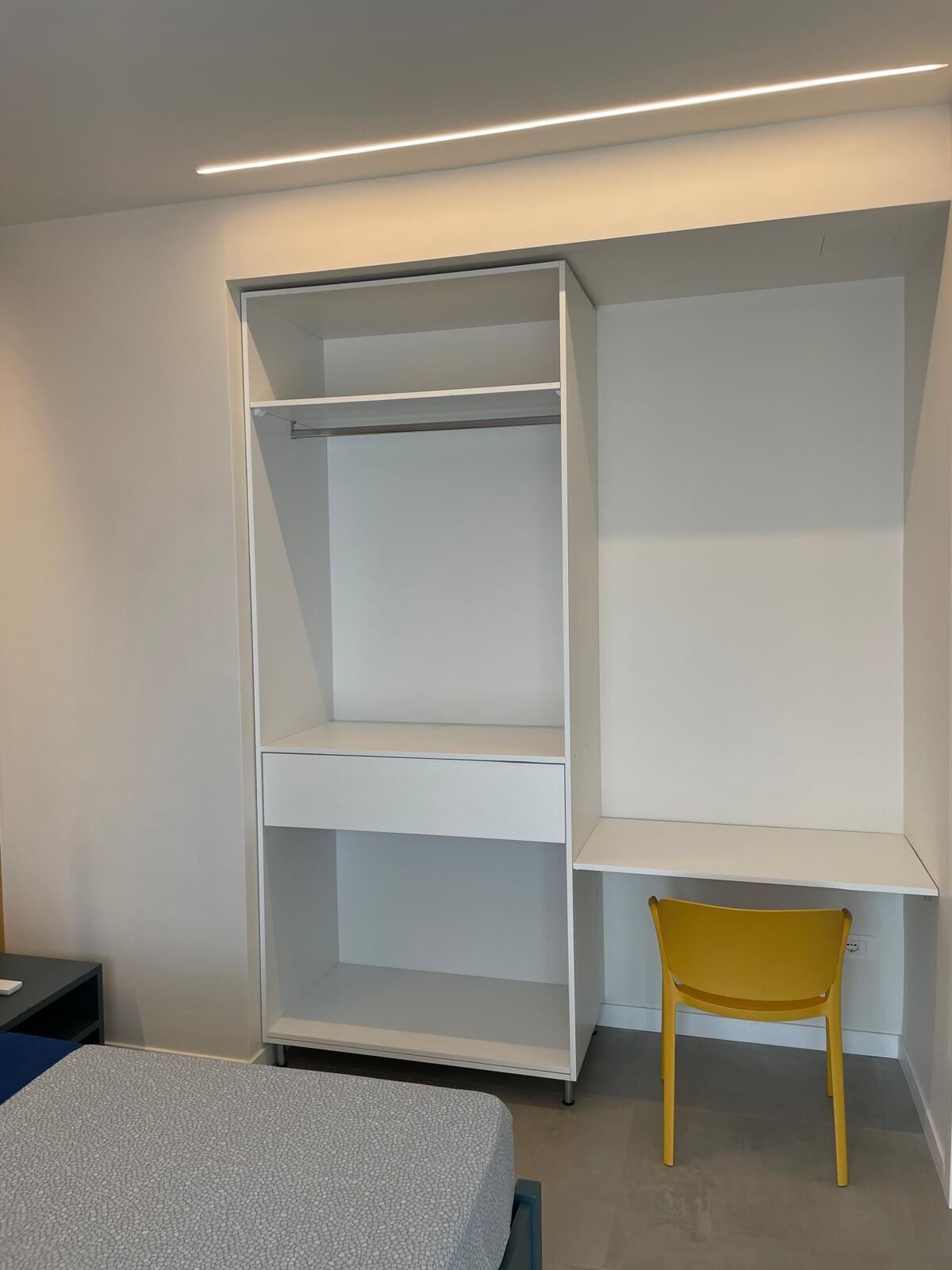 A room with a bed, a white wardrobe, and a yellow chair.