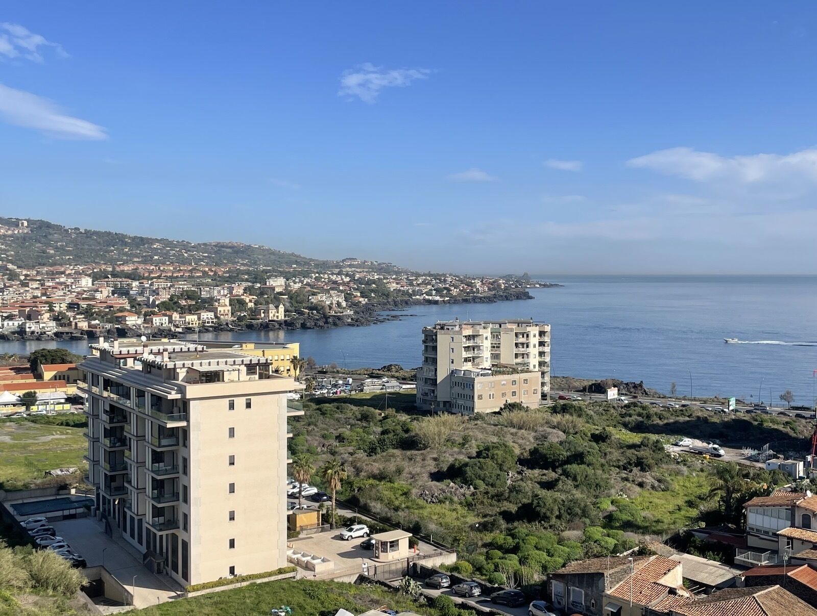 Un paisaje urbano costero con edificios modernos, un puerto deportivo y vistas al mar.