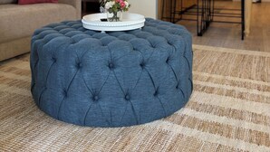 Una sala de estar con un reposapiés capitonado, un sofá y una mesa de centro con un arreglo floral.