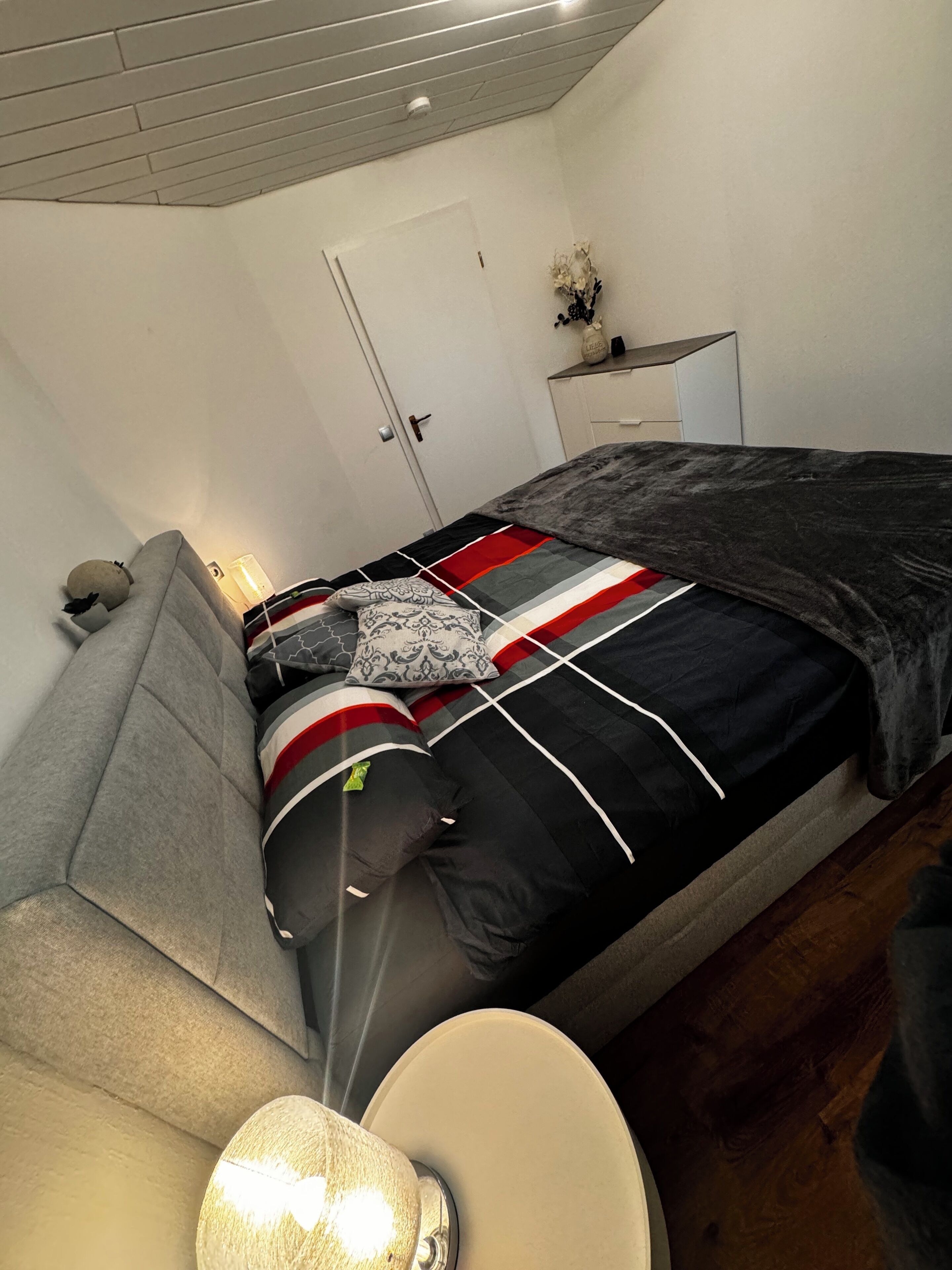 Une chambre à coucher avec un lit, un canapé, une table de chevet, une lampe et une porte.