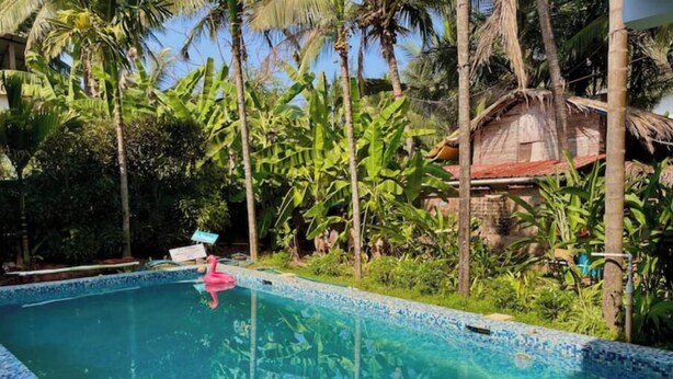 A swimming pool with a pink flamingo float, surrounded by lush greenery and a thatched-roof structure. - Sky Studio Apartment 03 Blue Sky Rentals
 (Canacona)