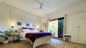 A bedroom with a bed, a nightstand, a potted plant, a ceiling fan, and a view of the outdoors. - Sky Studio Apartment 02 Blue Sky Rentals
 (Canacona)